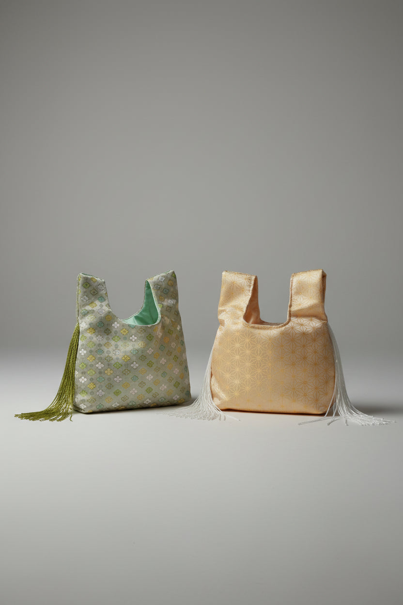 Two reusable tote bags with woven geometric patterns. The bag on the left is sage green and yellow, and the bag on the right is gold and white, both featuring tassel details.