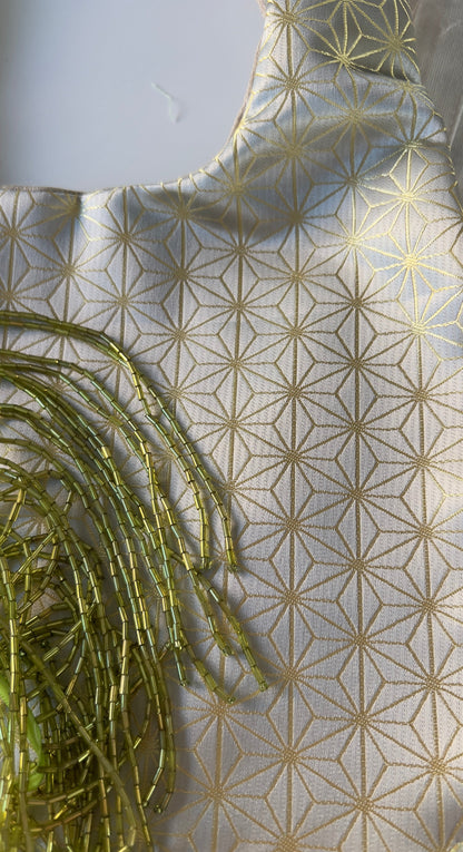 A close-up of a light beige fabric with a repeating gold geometric star pattern, featuring a tassel fringe detail on the left side.