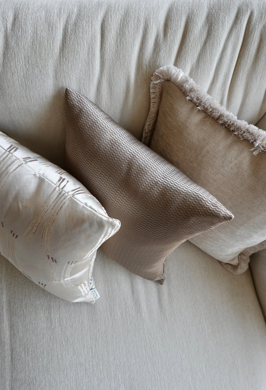 Three pillows on a beige sofa with textured cushions.