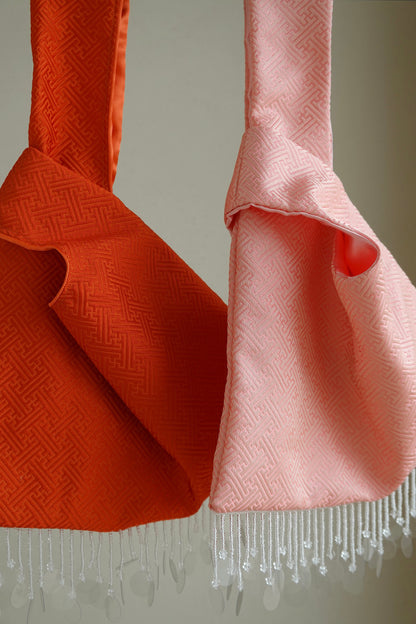 Two bags, one orange and one pink, with beaded fringe details 