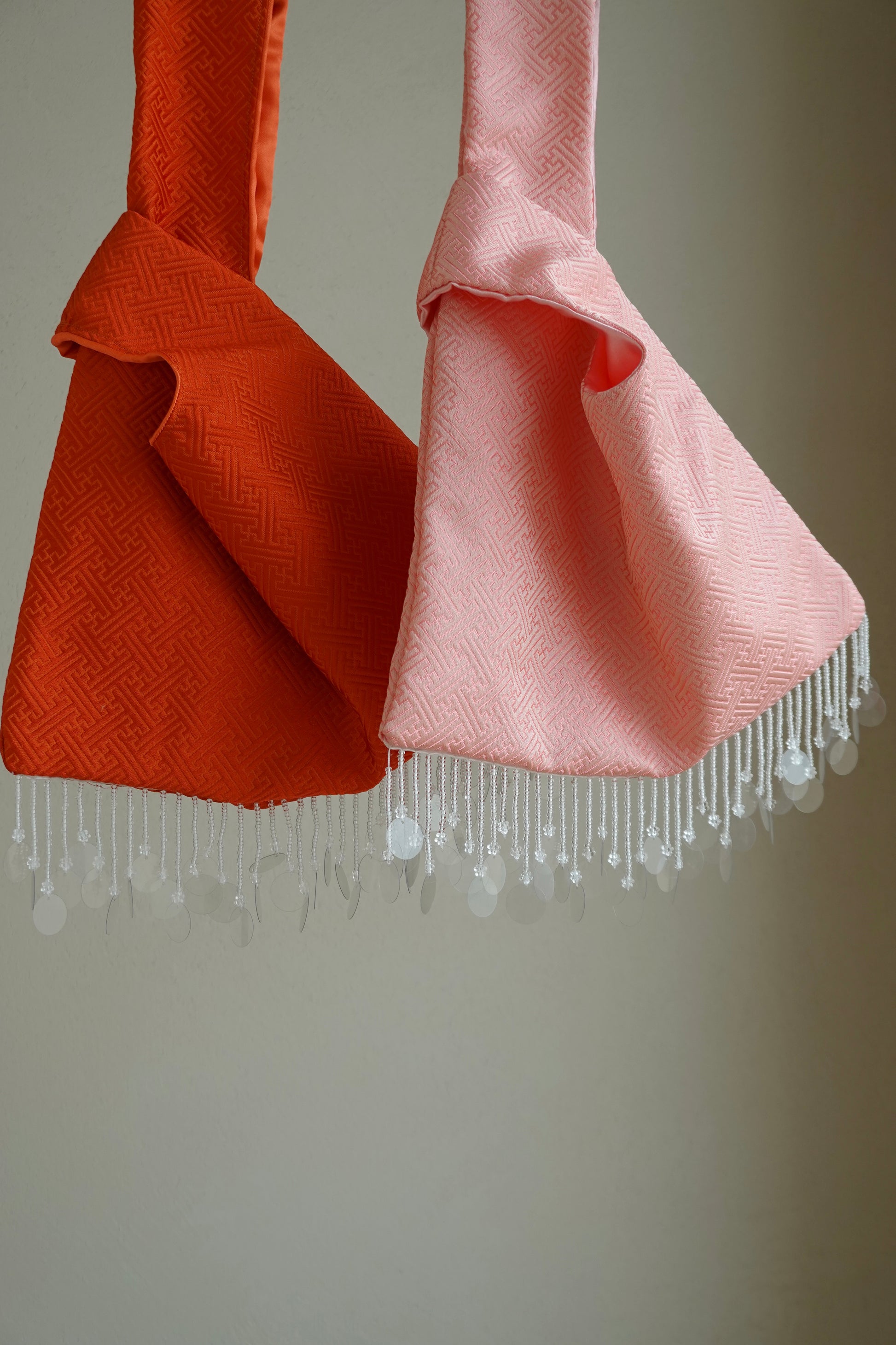 Two handbags, one orange and one pink with fringe
